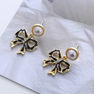 Détail de boucles d'oreilles papillon dorées avec émail noir et accents de perles blanches