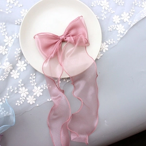 Pink tulle ribbon bow hair clip with long streamers on decorative lace background