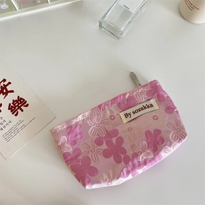 Detail of pink floral embossed makeup bag with zipper and woven brand label on white desk