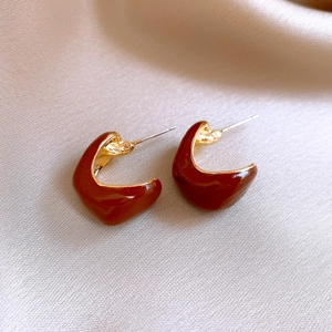 Close-up of vintage dark reddish-brown C-shaped earrings on champagne silk fabric