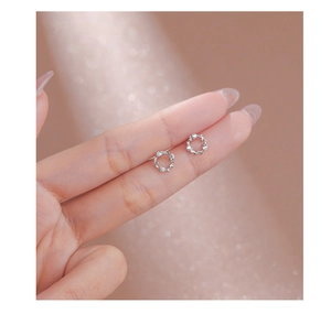 Macro shot of tiny silver floral wreath earrings with crystals held on a fingertip