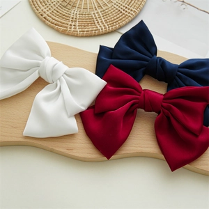 Flat lay of three satin bow hair clips in white, navy, and wine red on a wooden board