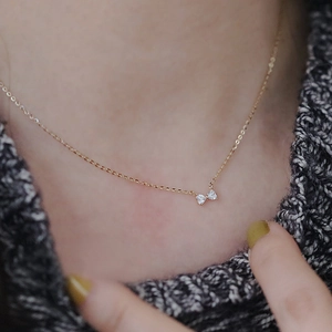 Close-up of a delicate 14k gold bow necklace with heart-shaped gems on a gray sweater