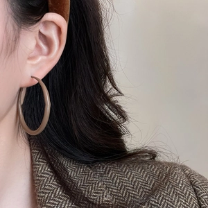 Close-up of a large beige geometric resin hoop earring worn by a model in a natural style