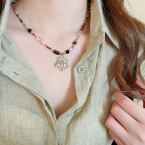 Detailed view of handmade beaded necklace with vintage gold floral pendant on model