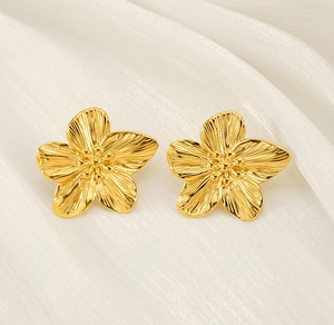Macro di orecchini a fiore in oro 18K con texture metallica spazzolata su seta bianca