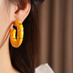 Close-up of a yellow enamel C-shaped hoop earring with gold bamboo texture on a model