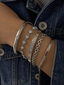 Détail de cinq bracelets argentés avec charmes cœur et zircon sur fond de veste en jean