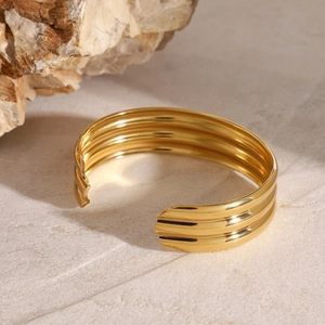 Polished gold multi-layer open cuff bracelet set on a textured stone surface