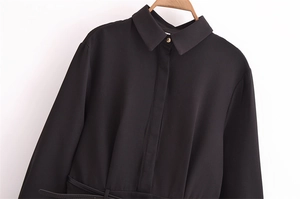 Detail of black long-sleeve shirt dress featuring classic collar and golden decorative button