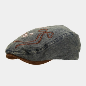 Detailed side view of dark blue denim beret with brown suede brim and embroidery