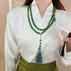 Détail du long collier en perles de jade avec accents dorés et gland en soie bleue