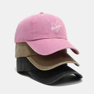Close-up of three washed cotton baseball caps in pink, khaki, and grey with Mama embroidery