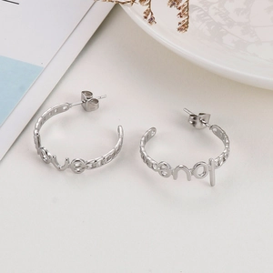 Macro detail of silver C-shape hoop earrings featuring love lettering and chain texture