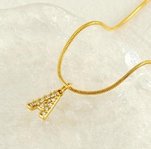 Macro shot of gold letter A pendant with shimmering stones on a sleek snake chain