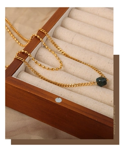 Detail of double-layer gold necklace with hexagonal green gemstone on silk background