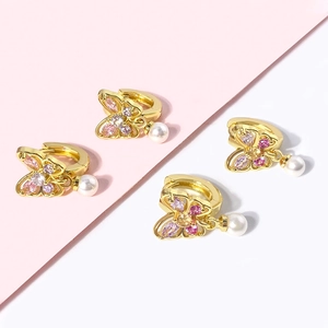 Détail de boucles d'oreilles papillon dorées avec zircons colorés et perles blanches