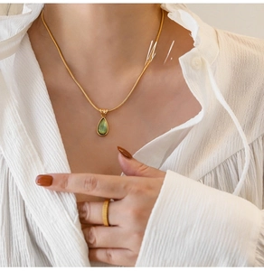Detail of a model wearing a gold snake chain necklace with an olive green drop pendant