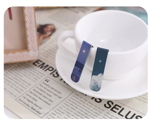 Scenic magnetic bookmarks with ocean and cloud patterns clipped on a white coffee cup