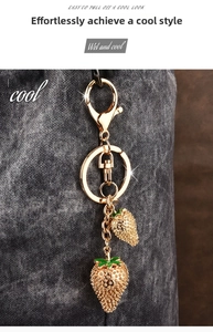 Detailed view of golden strawberry keychain with red enamel charms on a stylish bag