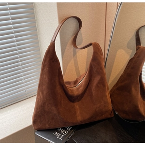 Detail of a large brown suede tote bag leaning against a wall in a minimalist interior
