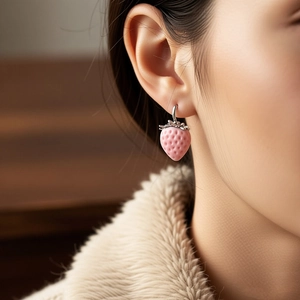Macro detail shot of a sweet pink flocked strawberry pendant earring on a model.