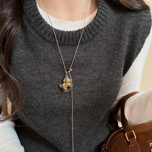 Détail d'un collier pendentif cheval à bascule doré avec cristaux sur un pull gris élégant