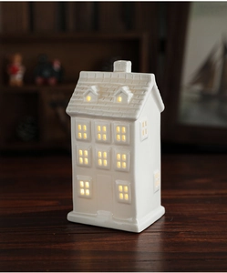 Close-up of white ceramic Christmas house with warm LED glowing through windows