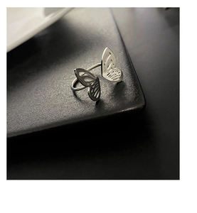 Macro shot of minimalist silver butterfly ring on dark textured tray with matte finish