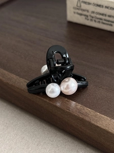 Détail d'une petite pince à cheveux noire ornée de trois perles blanches élégantes