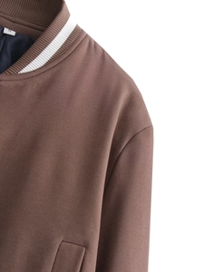 Dettaglio di giacca baseball marrone con colletto a righe bianche ed etichetta taglia S