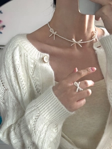 Close-up of woven white pearl bow necklace and matching ring on model for elegant style