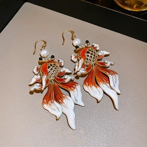 Detailed macro view of enamel goldfish earrings with pearl accents and golden frames
