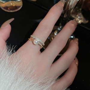 Dettaglio di un anello dorato a più strati con una perla e pietre di zircone cubico