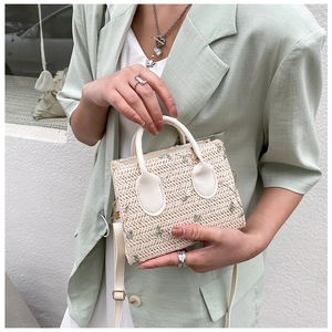 Detail view of woven straw tote with floral embroidery and white leather handles