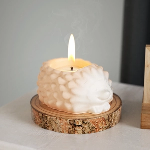 Close-up of lit hedgehog scented candle with detailed relief texture on a wood slice