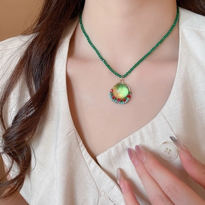 Detail of beaded necklace featuring a green stone pendant and crystal accents on neck