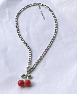 Silver chain necklace with red cherry pendant and white pearl on wrinkled white background