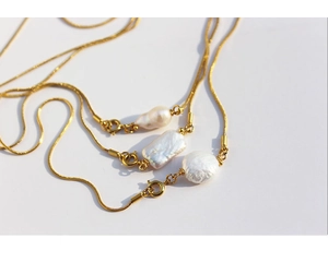 Detailed macro view of three gold snake chains featuring baroque and round pearl pendants