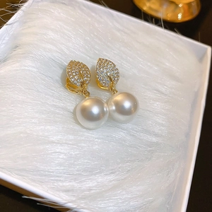 Detail shot of gold-plated leaf earrings with shimmering crystals and white pearls