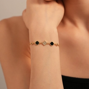 Detail of adjustable gold bracelet with black enamel and zircon rhombus charms on wrist
