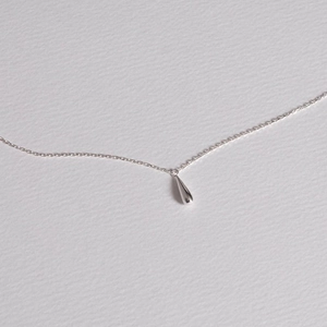 Close-up of minimalist silver water drop pendant necklace on a soft textured grey surface