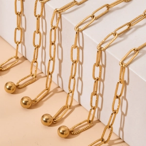 Close-up of golden paperclip link chain with polished spherical charms on white display
