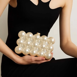 Detailed close-up of a pearl evening clutch with a gold clasp held by a model in black