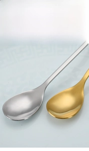 Detailed view of polished stainless steel leaf-shaped dessert spoons in gold and silver