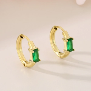 Gros plan détaillé de boucles d'oreilles créoles dorées avec verre vert émeraude