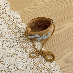 Close-up of a child's woven straw purse with three blue lace bows on a vintage lace mat