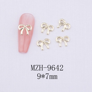 Detailed view of 9x7mm golden bow nail charms on a pink nail plate and white background