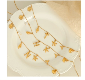 Detail of 18K gold-plated necklace with starfish, shell, and pearl charms on white plate
