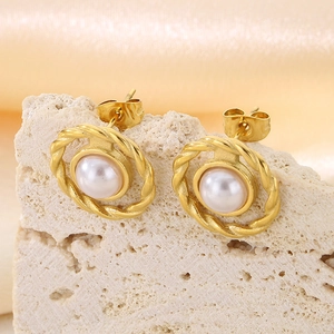 Macro shot of gold-plated circular earrings with white pearls on a textured stone surface